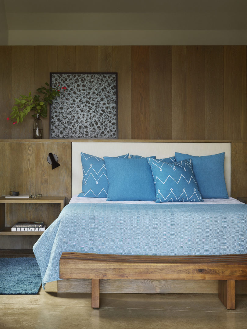 The master bedroom is done with a lot of natural wood, with a built in bed and a bench, with a pretty artwork
