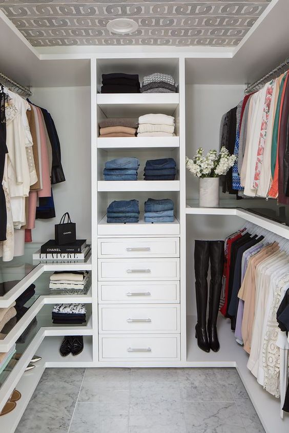 a small contemporary closet with open shelves, drawers, holders for hangers, glass shelves and a wallpaper ceiling