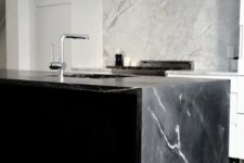 15 a minimalist white kitchen and a black kitchen island with a cool black marble countertop that echoes with a white marble backsplash