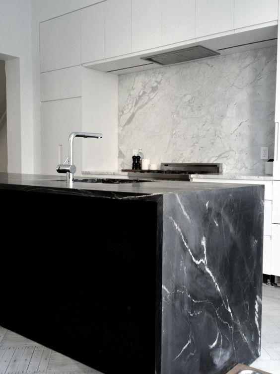 a minimalist white kitchen and a black kitchen island with a cool black marble countertop that echoes with a white marble backsplash