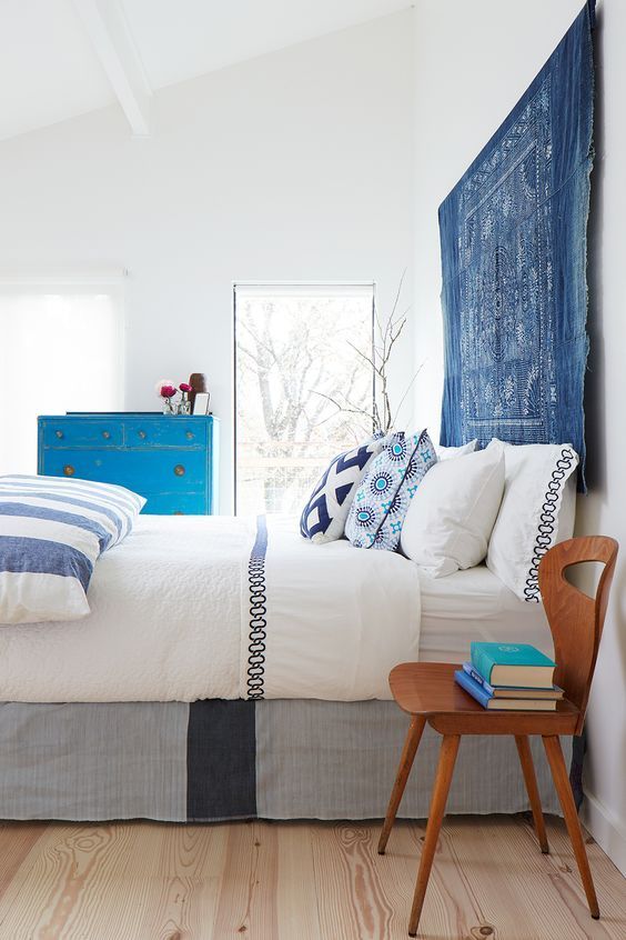 A bold and vivacious bedroom in white, with printed and colorful textiles, a blue tapestry instead of a usual headboard