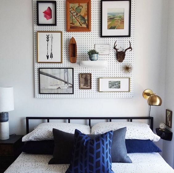 a white pegboard with artworks and potted greenery over the bed is a creative and cool alternative to a usual headboard