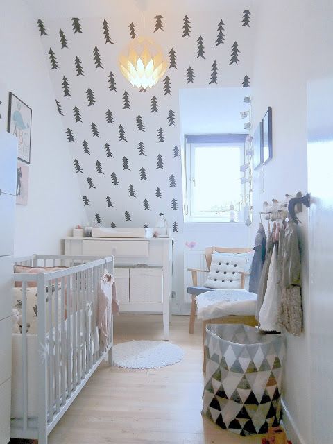 a Nordic nursery with a fir tree wall, a black and white can, neutral furniture and some artworks for an ambience