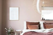 a beautiful attic bedroom with blush walls, a bed with contrasting bedding, a dark-stained wooden bench and a woven pendant lamp