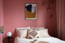 a beautiful pink bedroom with a shelf with decor and books, a bed with neutral bedding and a black nightstand with lamps
