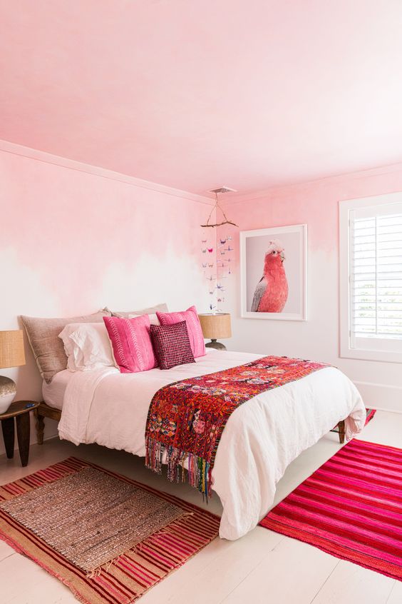 a bold bedroom with ombre pink walls, a pink ceiling, hot pink pillows and a rug plus a parrot artwork