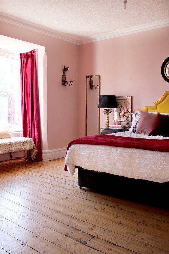 a bold whimsical bedroom with pink walls, fuchsia curtains, statement pillows, a black bed and lamps