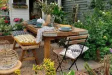 a bright and cool backyard with a lot of greenery, a wooden dining set and folding chairs, candle lanterns and blooms