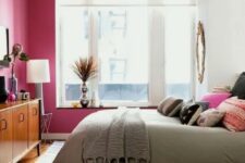 a bright and welcoming mid-century modern bedroom with a fuchsia statement wall, a rich stained dresser and a brass burst chandelier