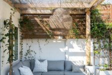 a bright boho patio with a corner sofa, some metal chairs, a concrete and marble table, a wicker pendant lamp and some greenery on the walls