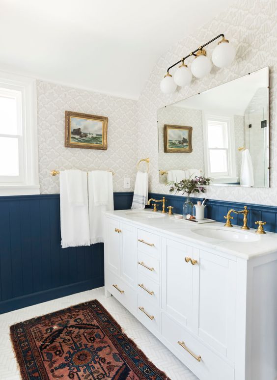 a bright eclectic bathroom with bold blue beadboard, neutral printed wallpaper, a white vanity and touches of brass