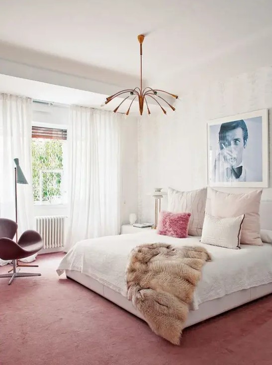 A bright mid century modern bedroom with a pink rug and chair, a copper chandelier, a large bed and an artwork