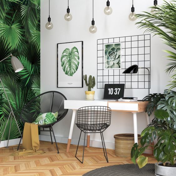 a bright tropical home office with a tropical leaf wall, lots of potted greenery, artworks, a woven basket and hanging bulbs