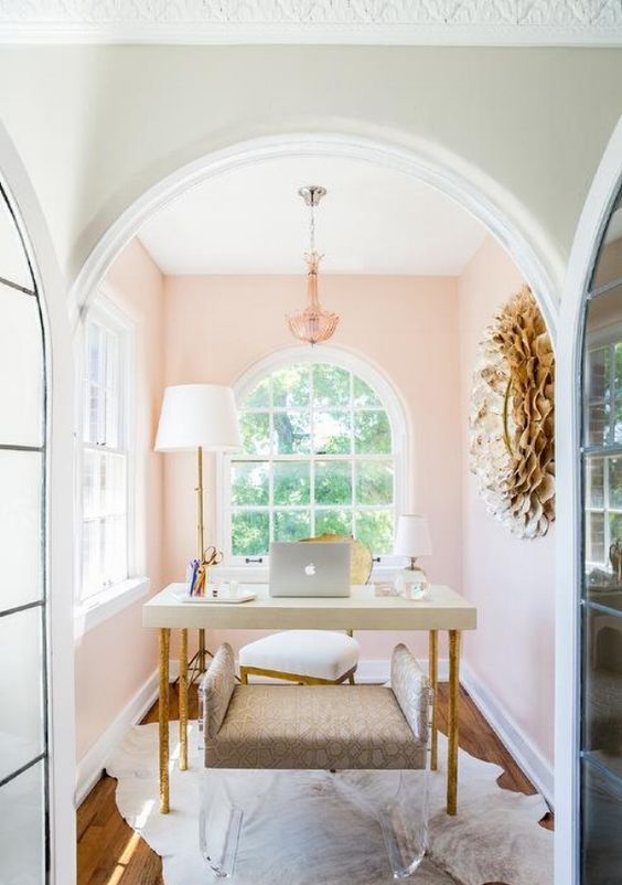 a chic and cozy home office nook with light pink walls, a chic chandelier, a simple desk and an upholstered and acrylic bench