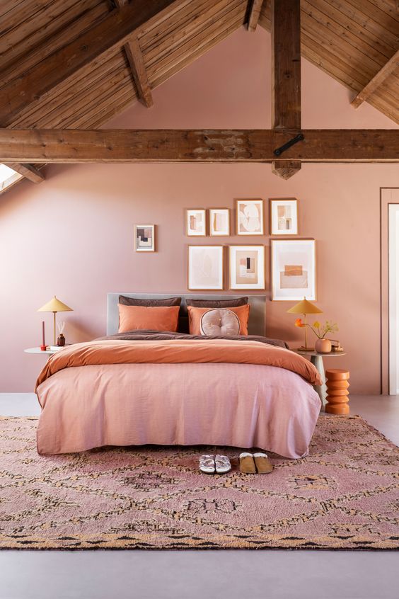 a chic attic pink bedroom with a bed and colorful bedding, a pink printed rug, a gallery wall and nightstands with table lamps