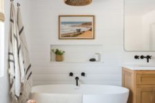 a chic beach bathroom done with a white beadboard wall, hex tiles, a wicker lamp and a wooden vanity plus touches of black