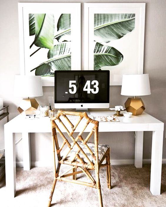 a chic tropical home office nook with a rattan chair, gold table lamps, tropical artworks and a white desk