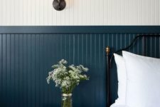 a chic vintage-inspired bedroom with white and navy beadboard fully covering the wall, a black forged bed and a wooden nightstand