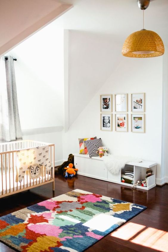 a colorful attic nursery with a pink ceiling, a gallery wall, bright printed textiles and a wicker pendant lamp