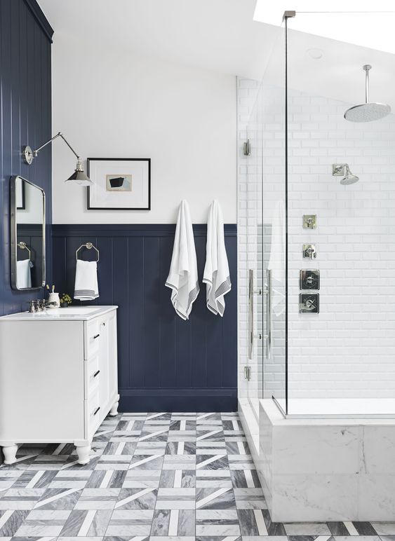 a contrasting bathroom with white tiles, navy beadboard, a skylight and printed tiles on the floor plus a white vanity