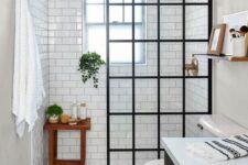 a contrasting black and white bathroom with white subway tiles and printed tiles, a black vanity, a framed screen and brass touches