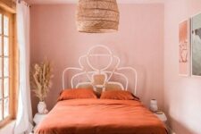 a cool boho pink bedroom with a rattan and cane bed, a large woven pendant lamp, a gallery wlal and a printed rug