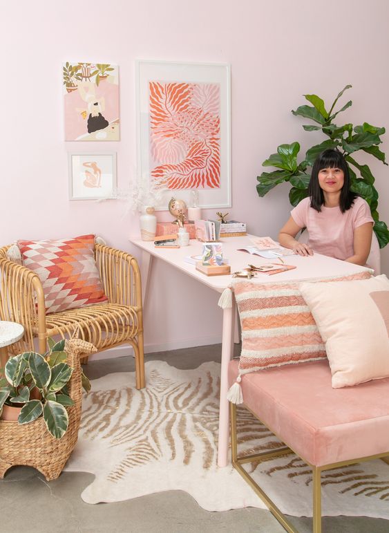 a cool glam home office with light pink walls, a pink chair, a pink gallery wall and a bright printed pillow
