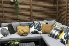 a cool small patio with wooden privacy screens, a corner sofa with bold pillows, a black coffee table and some decor