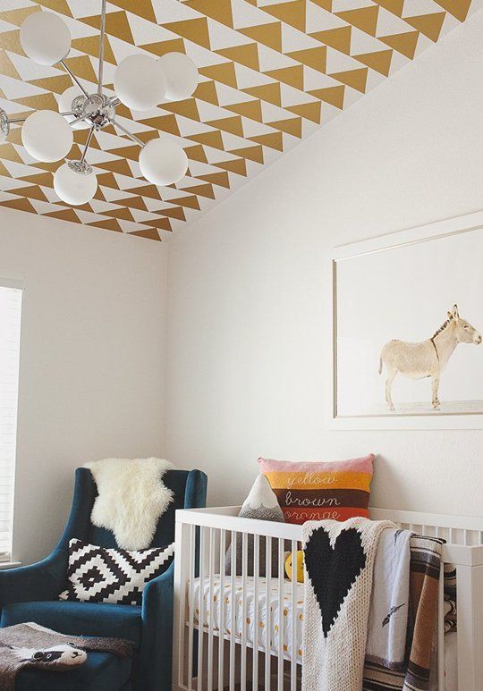 a cozy nursery with a geometric printed ceiling, bright printed textiles, a blue chair and a fun artwork