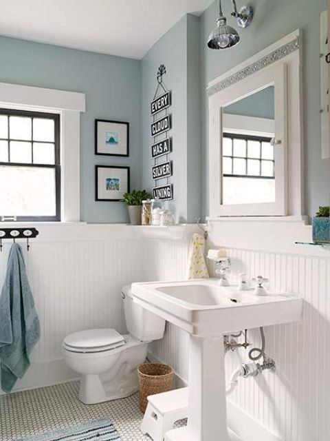 A cozy vintage farmhouse bathroom with light blue walls, white beadboard, a free standing sink, some art and much light