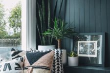 a cozy window nook with a black beadboard wall, a windowsill daybed and a large window plus potted plants