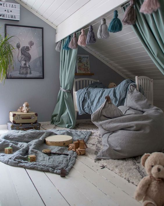 a creative attic nursery with muted color textiles, layered rugs, a tassel garland, artworks and lots of toys