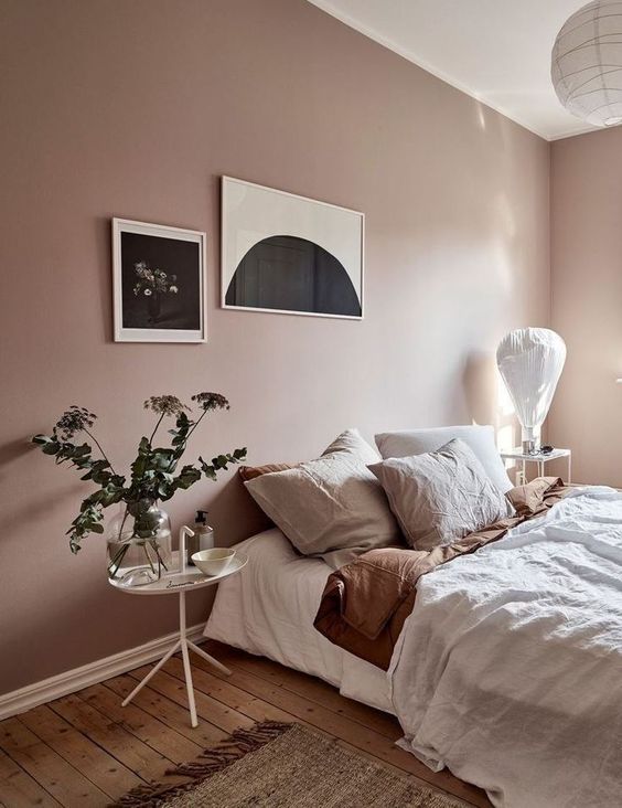 a dreamy bedroom with blush walls, muted color bedding, greenery and a monochromatic gallery wall