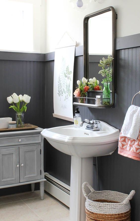 A farmhouse bathroom with black beadboard, vintage furniture, a free standing sink and some blooms and greenery