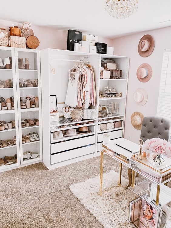 a girlish cloffice with a white makeshift closet, hats on the wall, a crystal chandelier, a catchy acrylic desk and a storage unit