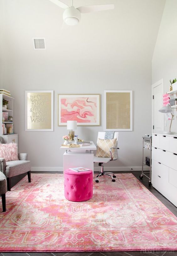 a glam home office with a pink printed rug, gold and pink gallery walls, a hot pink ottoman and a fluffy pillow