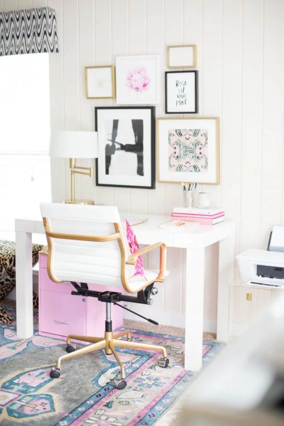 A modern home office with touches of pink   in the gallery wall, books, a pillow and a storage unit under the desk