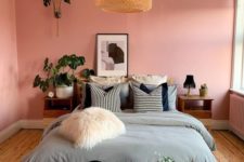 a modern meets boho bedroom with pink walls, wooden furniture, a wicker lamp, potted greenery and a faur fur pillow