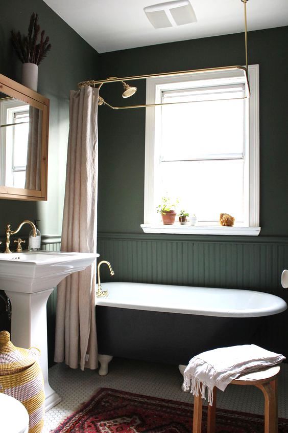 A moody vintage inspired bathroom with hunter green walls and beadboard, a black tub, a tile floor and a free standing sink plus touches of brass