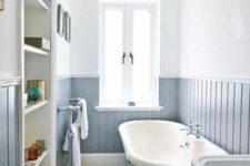 a neutral and welcoming bathroom with powder blue beadboard, printed tiles, a built-in storage unit and a blue tub