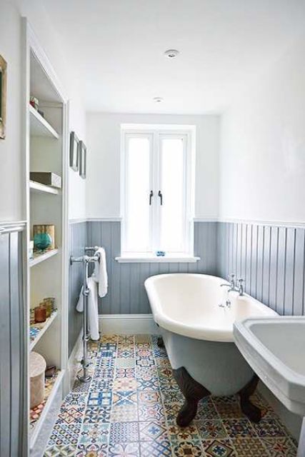 A neutral and welcoming bathroom with powder blue beadboard, printed tiles, a built in storage unit and a blue tub