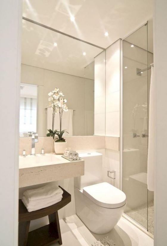 a neutral minimalist bathroom with a large mirror, a square sink, a shower space and a dark stained wooden stool