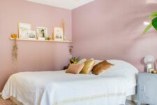 a pink bedroom with a bed and neutral bedding, a boho rug, a ledge gallery wall, a metal cabinet and a pendant lamp