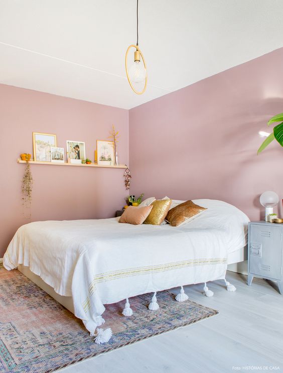 a pink bedroom with a bed and neutral bedding, a boho rug, a ledge gallery wall, a metal cabinet and a pendant lamp