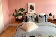 a pink boho bedroom with a bed and grey bedding, a rattan bench, stained nightstands and potted plants
