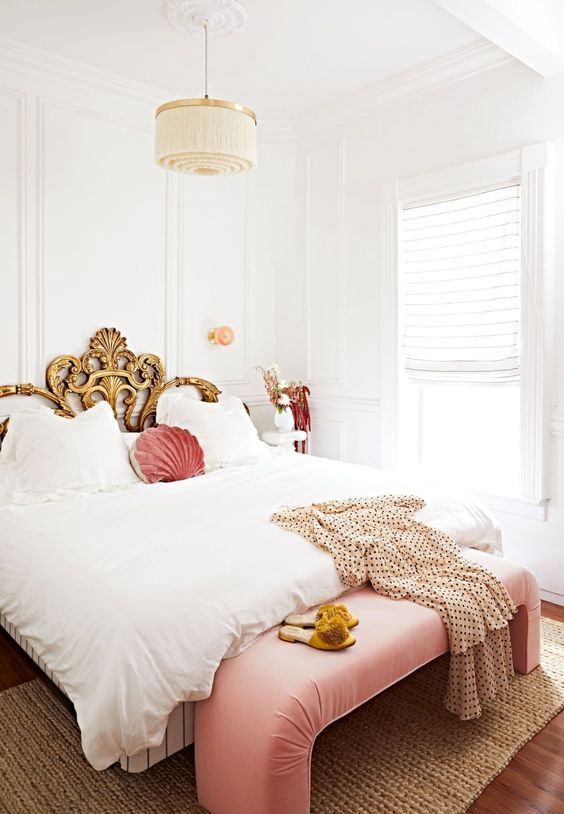 a refined bedroom in neutrals, with a gold exquisite bed, a pink bench and pillow plus a tassel chandelier