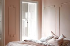 a refined vintage-inspired bedorom with blush molding walls, blush and white bedding, a wooden floor and a paper lamp