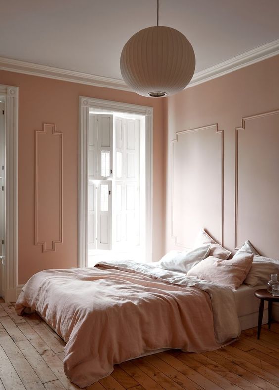 a refined vintage inspired bedorom with blush molding walls, blush and white bedding, a wooden floor and a paper lamp