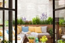 a small and bright patio with a corner sofa with lots of pillows, a couple of benches and blooms and greenery around