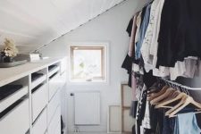 a small and cool attic closet with a dresser, railings for clothes, a printed rug and some art is a smartly organized space